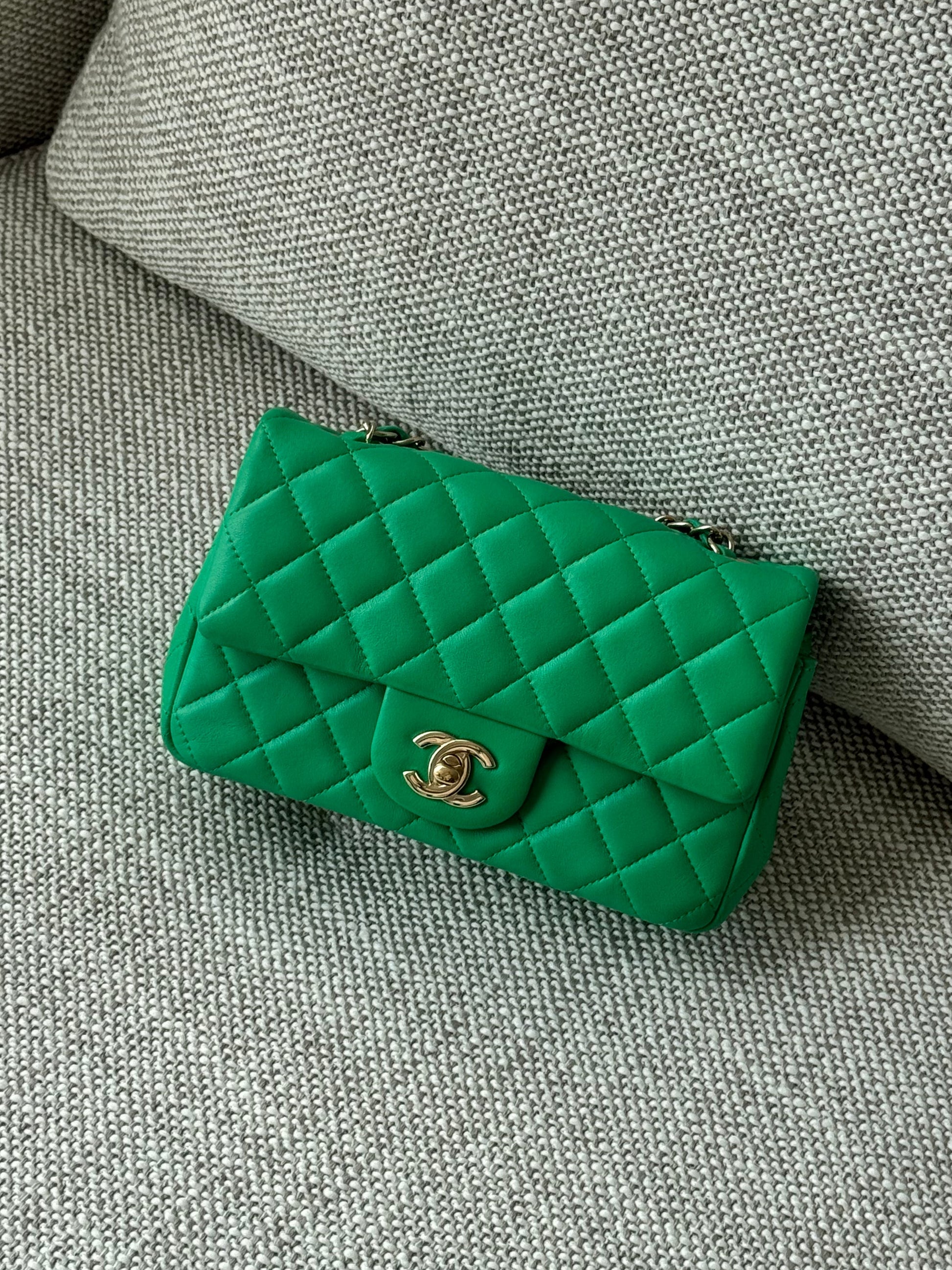 A green quilted Chanel flap bag with a gold CC turn-lock clasp, resting on a textured gray fabric surface.