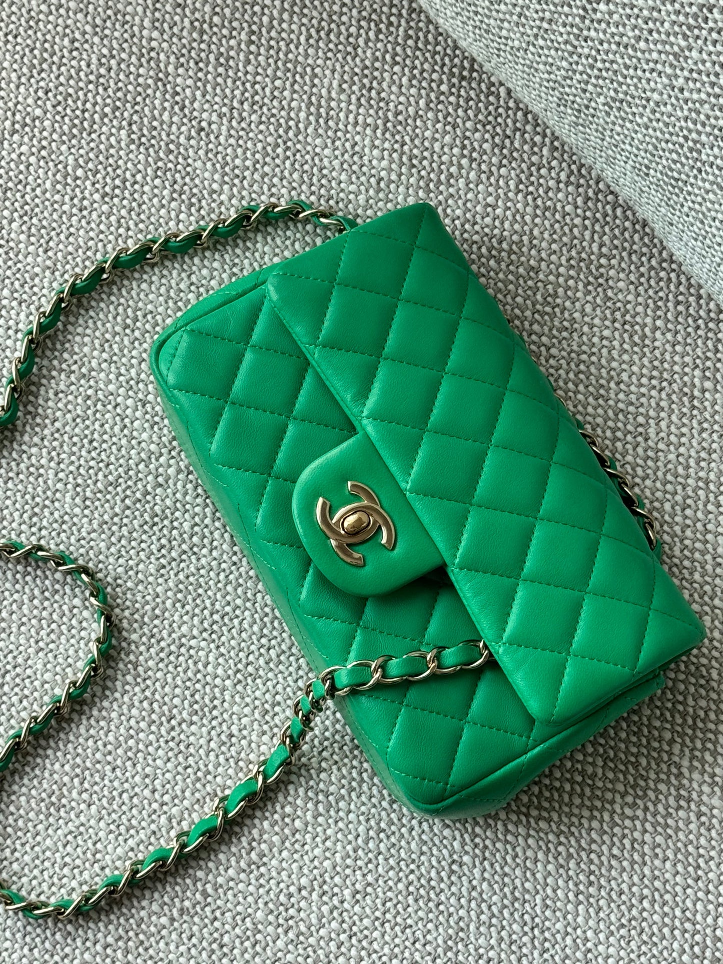A green quilted leather shoulder bag with a gold-tone interlocking CC logo, resting on a textured gray fabric surface.