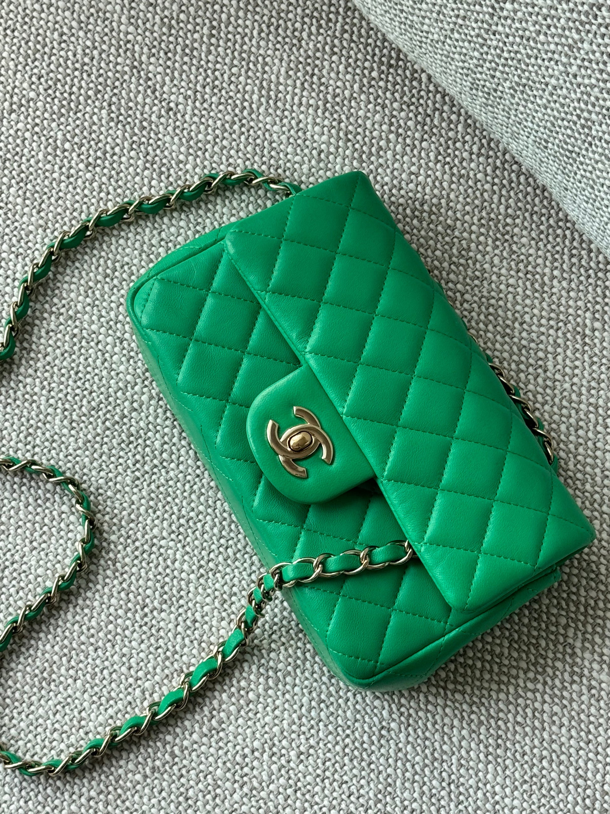 A green quilted leather shoulder bag with a gold-tone interlocking CC logo, resting on a textured gray fabric surface.